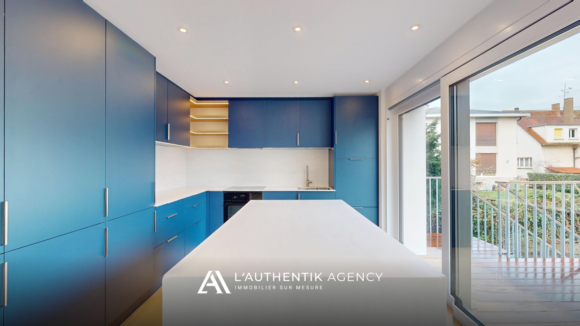 Cuisine équipée bleue avec îlot, attenante à la salle à manger et donnant accès à la terrasse